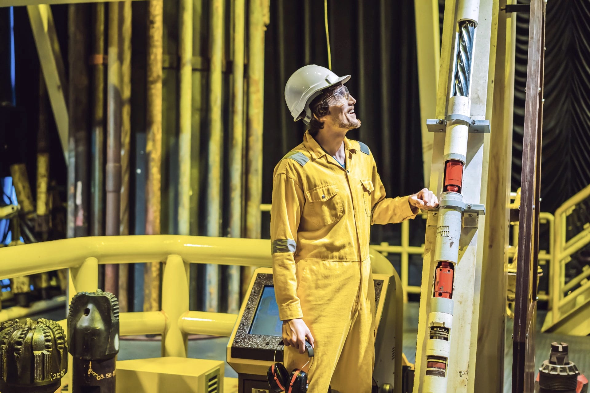 A worker in yellow coveralls and a hard hat on an offshore platform, among yellow pipework.
